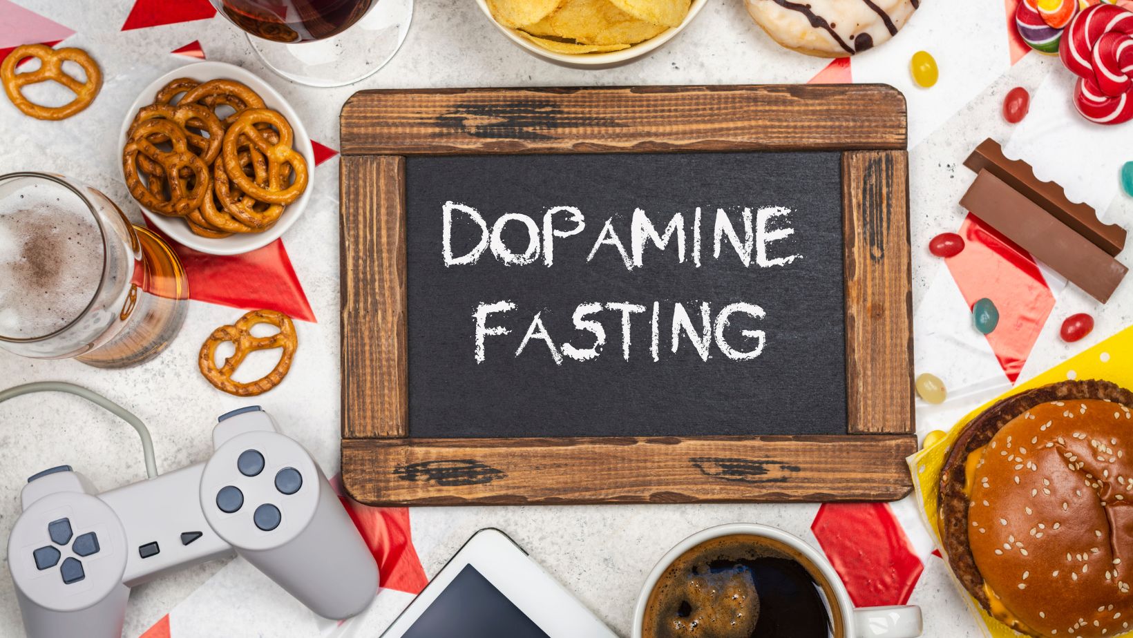 napis dopamine fasting na tablicy a wokół przykłady rzeczy prowadzących do uzależnienia od dopaminy - pad do konsoli, słodycze, słone przekąski, telefon, alkohol