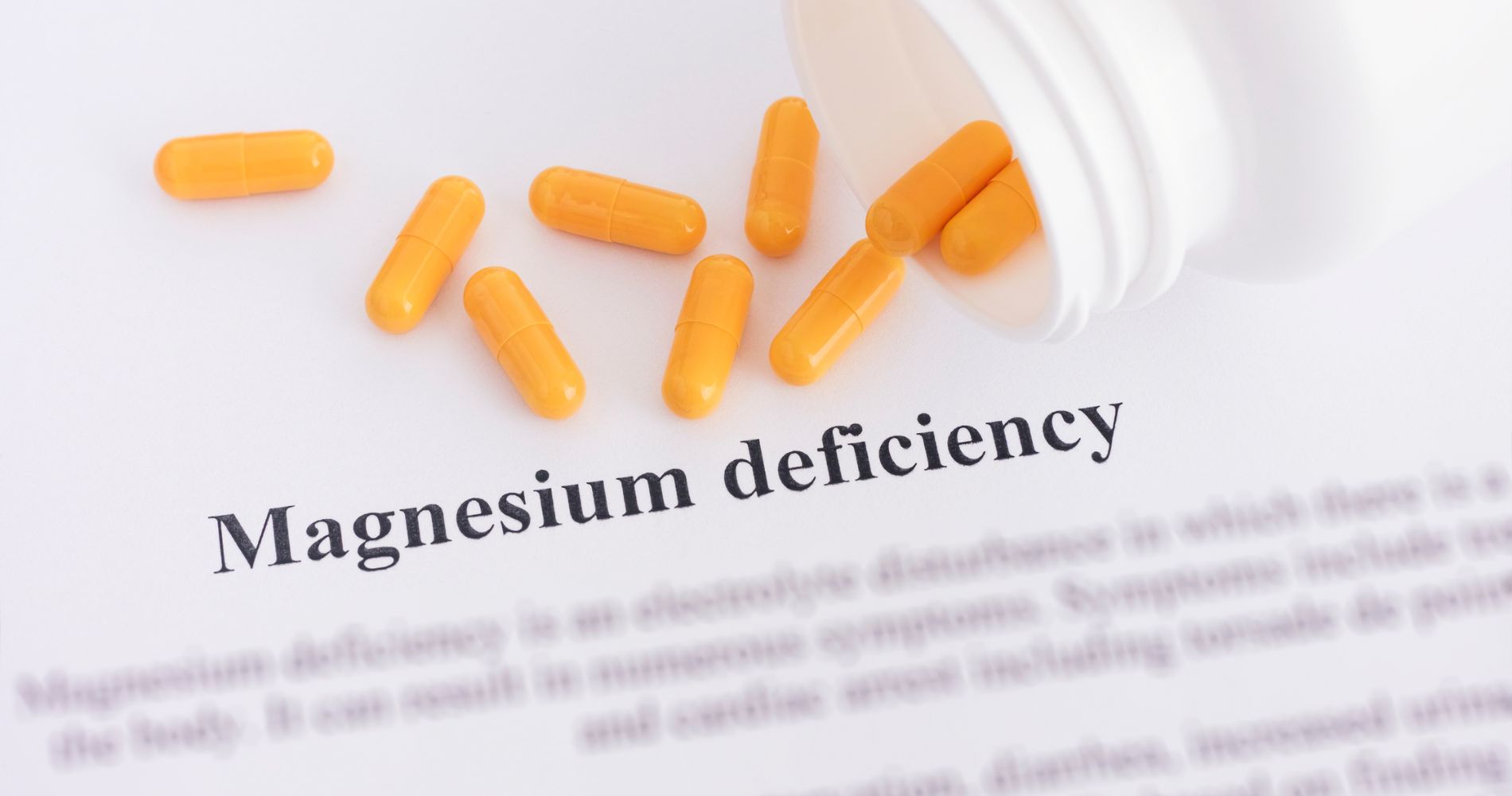 Pomarańczowe kapsułki wysypujące się z opakowania na kartkę z napisem "Magnesium deficiency".