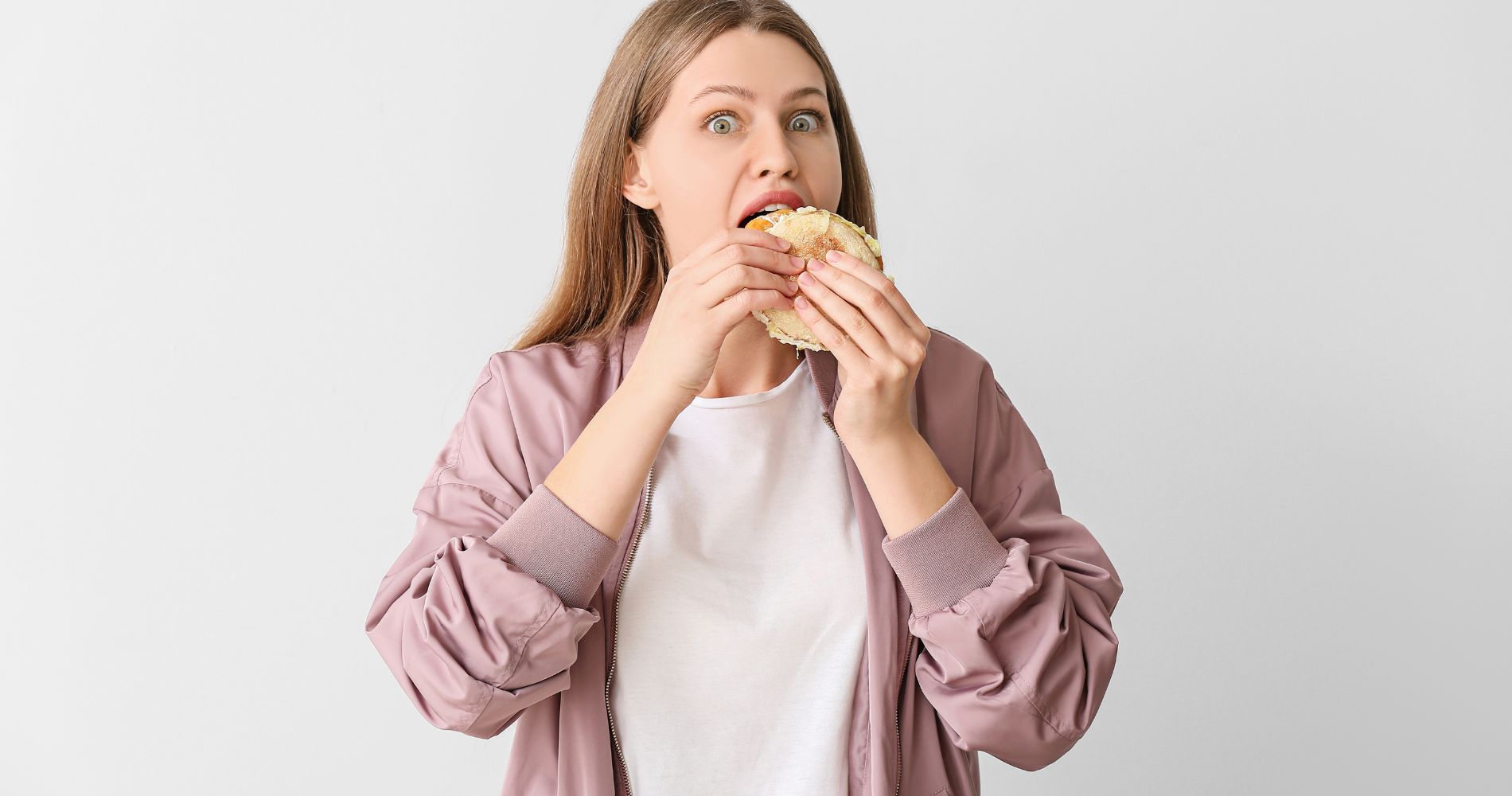 Kobieta jedząca hamburgera – objawy insulinooporności, takie jak nadmierny apetyt i trudności z kontrolą głodu.