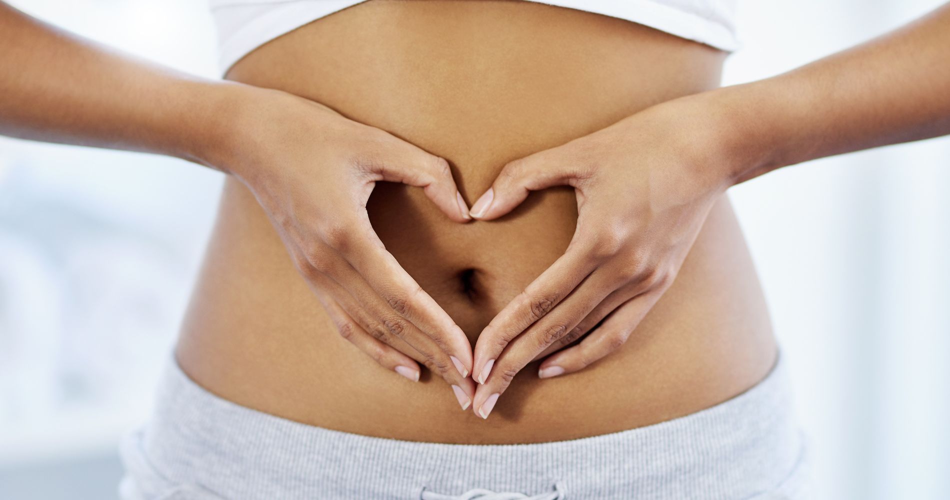 Nieszczelne jelita – kobieta trzymająca dłonie w kształcie serca na brzuchu jako symbol zdrowia układu pokarmowego.
