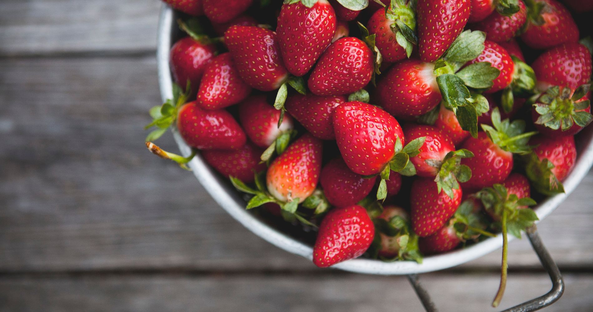 Miska pełna świeżych truskawek na drewnianym stole.