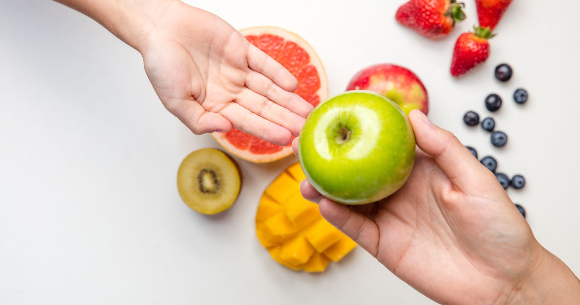 Zdrowe nawyki żywieniowe – podawanie dziecku jabłka w otoczeniu świeżych owoców.