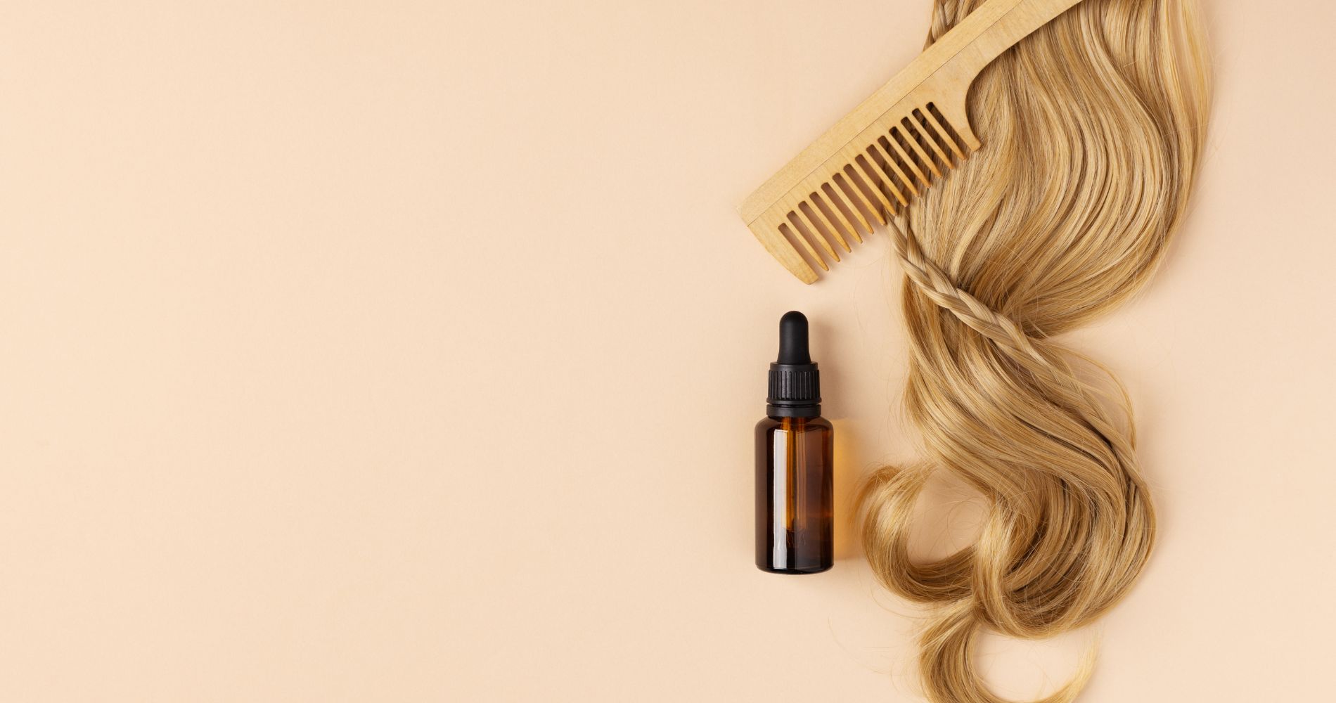 Buteleczka z serum, drewniany grzebień i pasmo blond włosów – pielęgnacja i wsparcie porostu włosów.