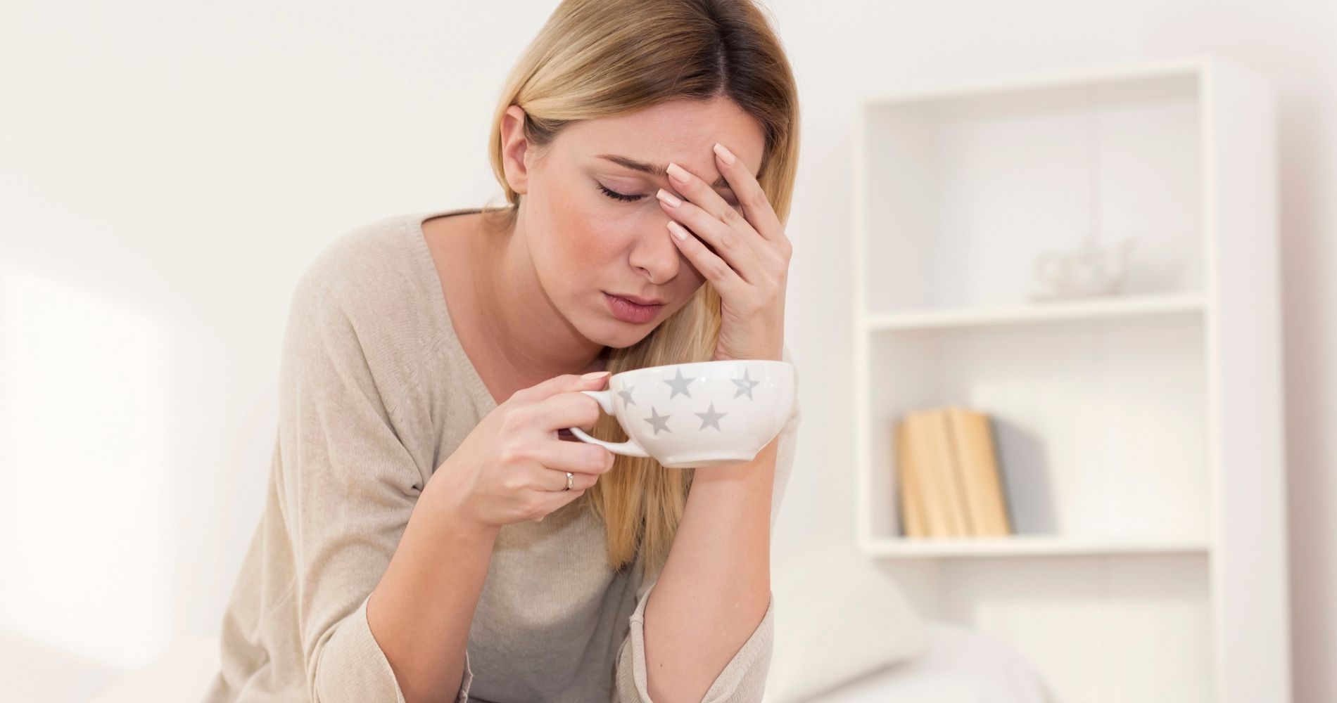 Kobieta odczuwająca zmęczenie i napięcie przed miesiączką, trzymająca kubek w dłoni – objawy PMS.