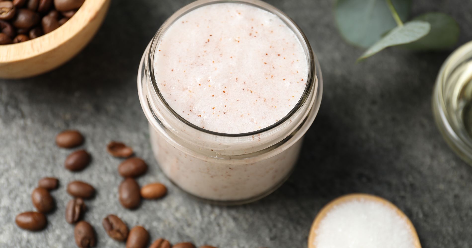 Domowy peeling do ciała w słoiczku na tle ziaren kawy.